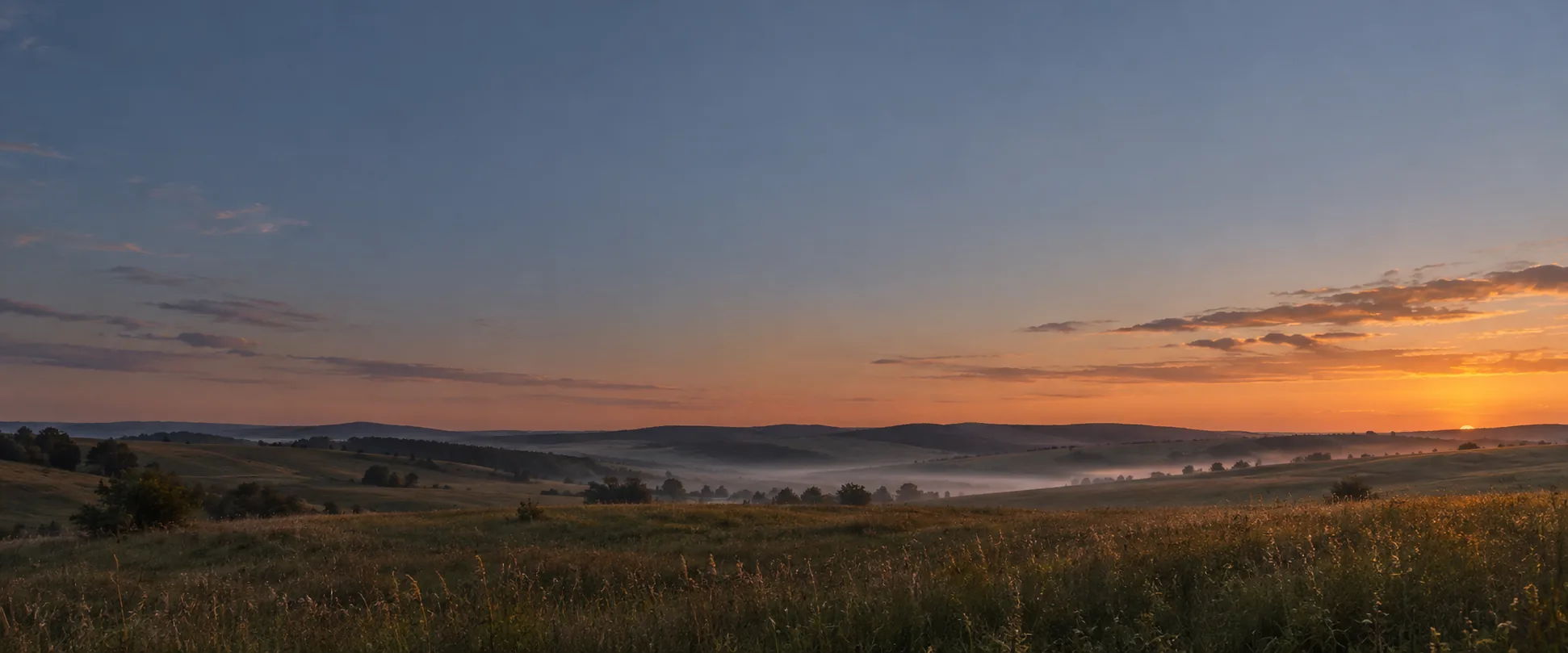Rolling meadow hills and evening mist at sunset