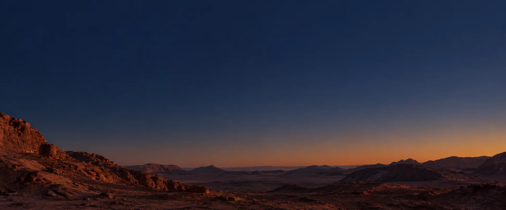 Rust-red desert ridges beneath a deep blue twilight sky