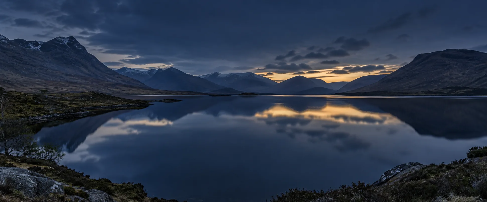 Still Highland lake and layered mountains at blue hour
